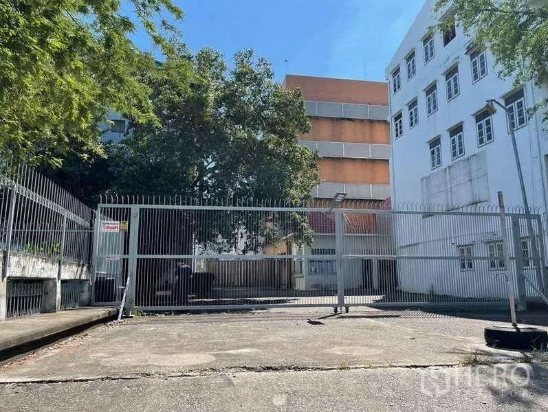 Factory for rent in Phra Samut Chedi, Samut Prakan - Wide driveway and sliding metal gate between white and orange factory buildings.
