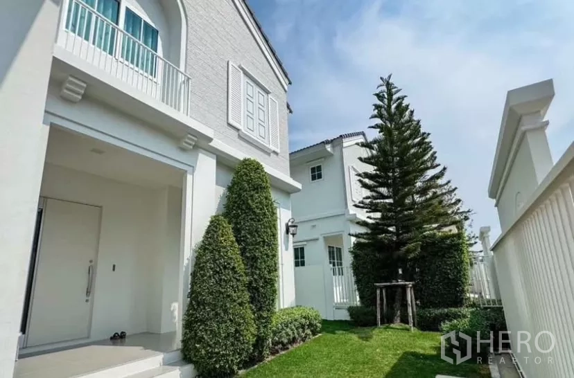 独立式住宅 出租在Bang Phli, Samut Prakan - 前院草坪与修剪整齐的绿篱及高大常青树。