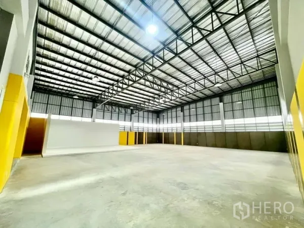 Warehouse for sale in Lam Luk Ka, Pathum Thani - Open factory floor with polished concrete, skylight panels and yellow accent walls along the perimeter.
