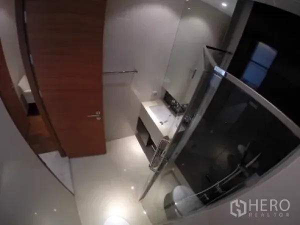 Condominium for rent in Khlong Toei, Bangkok - Contemporary bathroom with glass shower enclosure, vanity sink, and wall-mounted toilet.