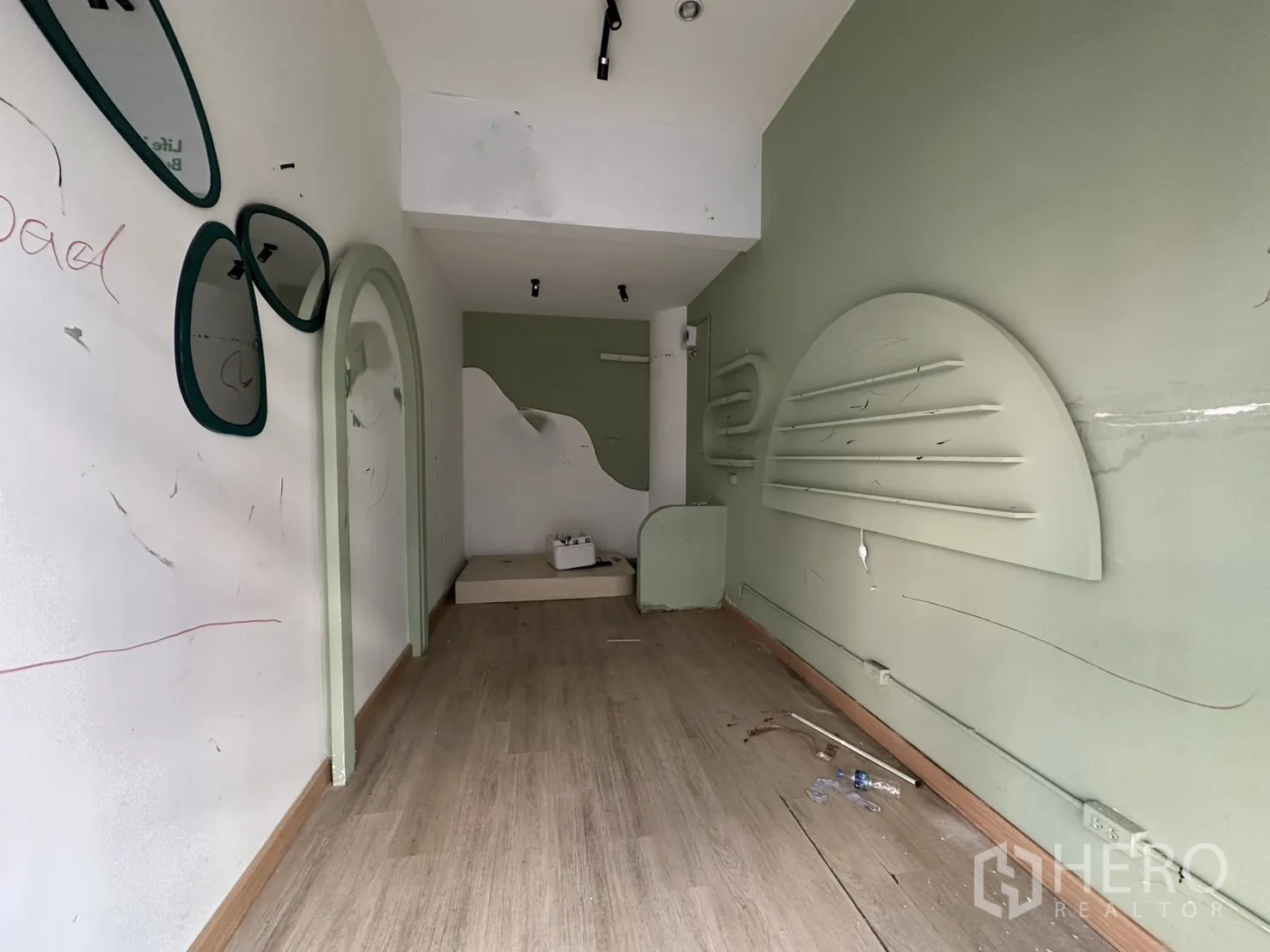 พื้นที่ขายของ for rent in Khlong Toei, Bangkok - ภายในร้านค้าทรงลึก พื้นลามิเนตสีไม้ ผนังสีเขียวพาสเทล ช่องโค้ง กระจกตกแต่ง และชั้นโชว์ติดผนัง