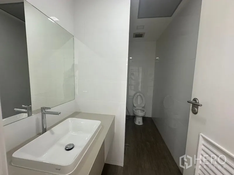 Office Space for rent - Clean bathroom featuring wide vanity sink, wall mirror, and enclosed toilet area.