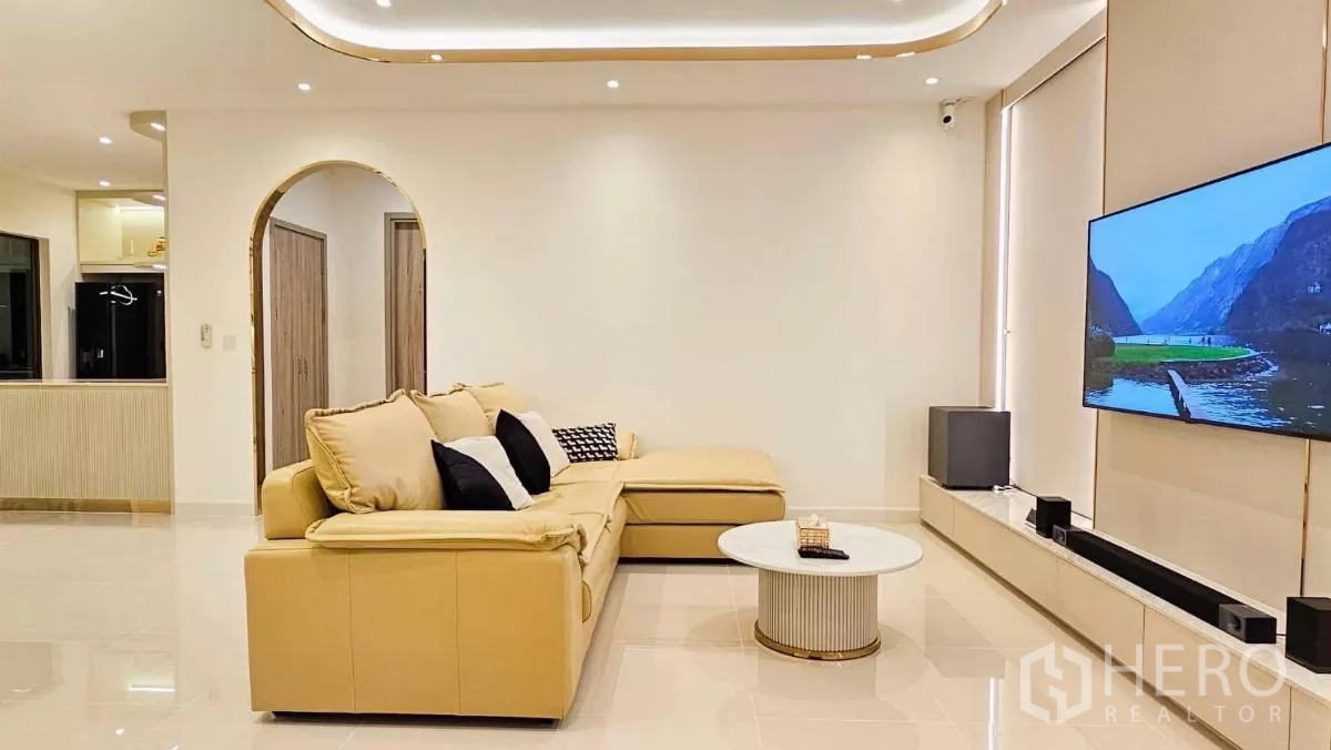 Detached House for rent or sale in Prawet, Bangkok - Bright living room with L-shaped leather sofa, wall-mounted TV, recessed lighting and glossy tile floor.
