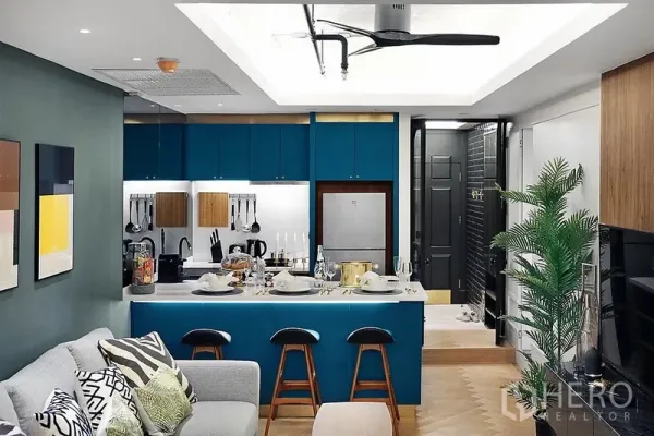 Condominium for rent in Bang Rak, Bangkok - Open-plan condo kitchen with teal cabinets, breakfast island set for dining, and a cozy living area beneath a ceiling fan.