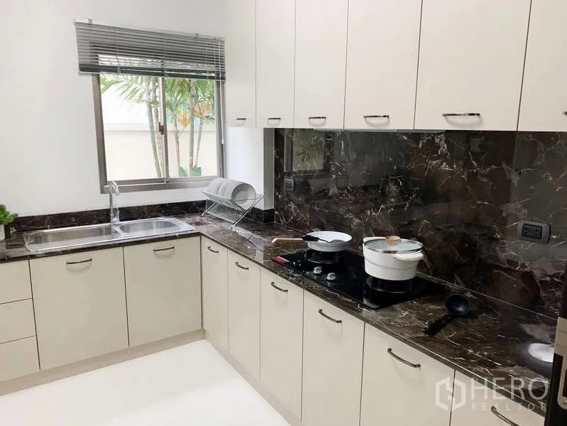 Detached House for rent or sale in Bang Phli, Samut Prakan - Separate Thai kitchen with L-shaped cabinets, dark marble backsplash and window.