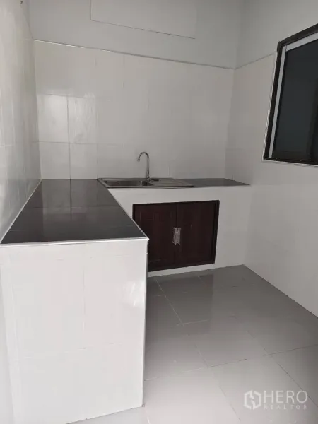 Townhouse for sale in Phra Khanong, Bangkok - Simple Thai kitchen with tiled counters, sink and window ventilation.