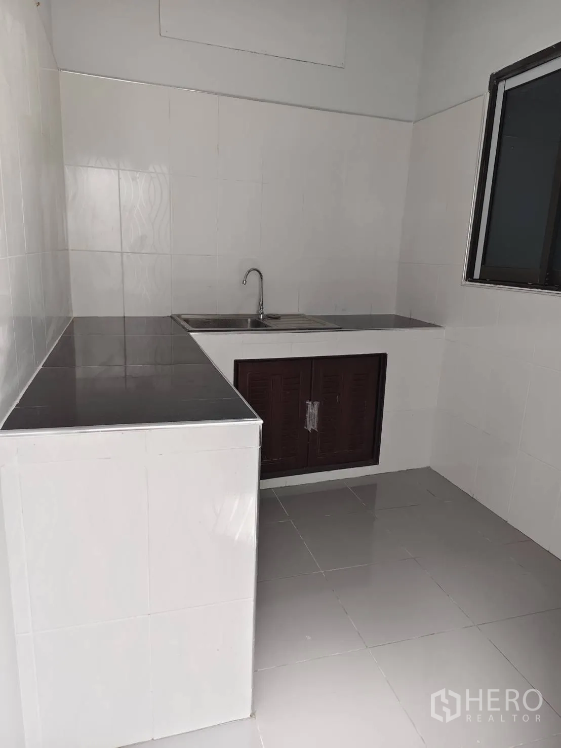 Townhouse for sale in Phra Khanong, Bangkok - Simple Thai kitchen with tiled counters, sink and window ventilation.
