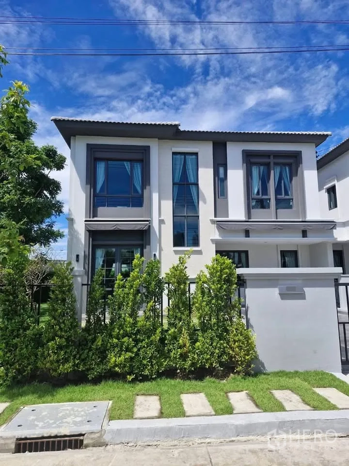 独立式住宅 for rent in Bang Phli, Samut Prakan - 现代两层独栋外立面，高窗与前庭绿篱，蓝天下格外醒目。