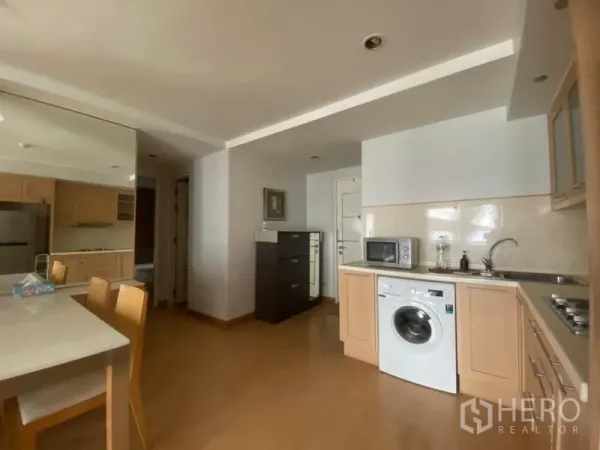 公寓 出租在Watthana, Bangkok - 紧凑厨房，浅木色柜体，配微波炉与洗衣机，紧邻入户走廊。