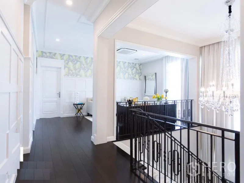 Detached House for rent in Mueang Samut Prakan, Samut Prakan - Upstairs hallway with dark wood floors, crystal chandelier and wrought‑iron stair railing.