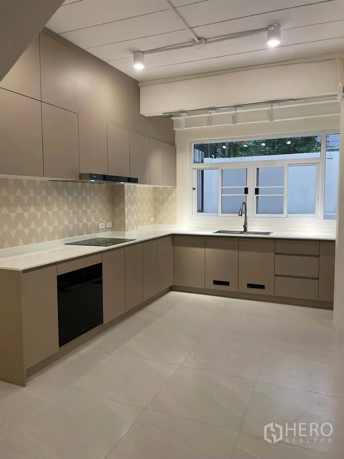 Townhouse for rent in Huai Khwang, Bangkok - Contemporary U-shaped kitchen with ample cabinetry, cooktop, oven, and window.