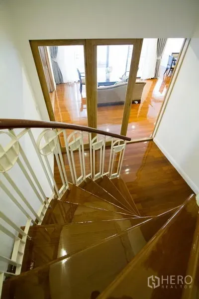 Apartment for rent in Watthana, Bangkok - Curved wooden staircase descending toward a bright living room with glass doors and polished floors.