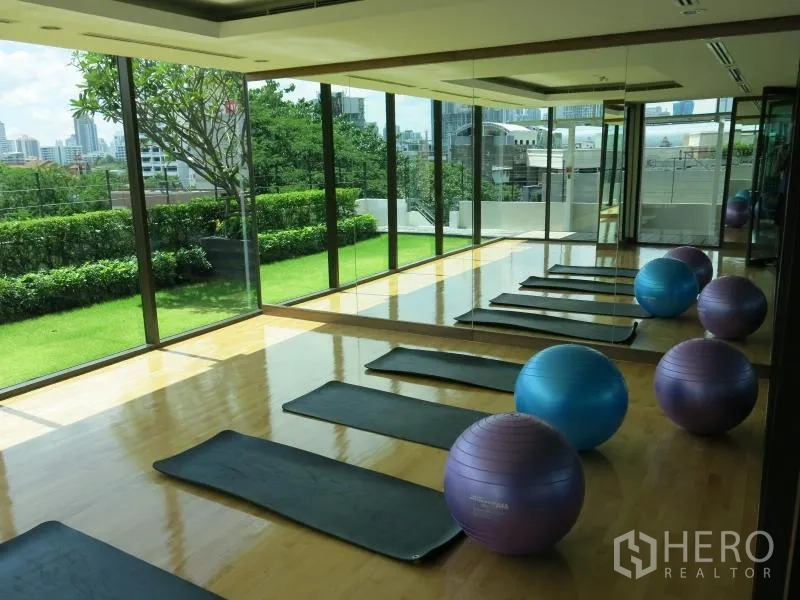 Condominium for rent in Ratchathewi, Bangkok - Glass-walled fitness and yoga studio overlooking a green garden with mats and exercise balls.
