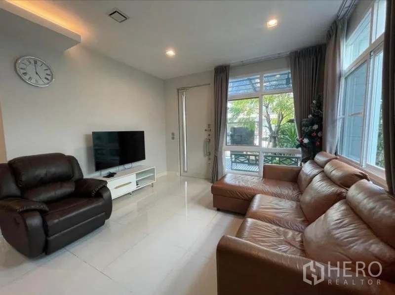 Detached House for rent in Lat Krabang, Bangkok - Living room with leather sofa set, TV, bright windows and white tile flooring