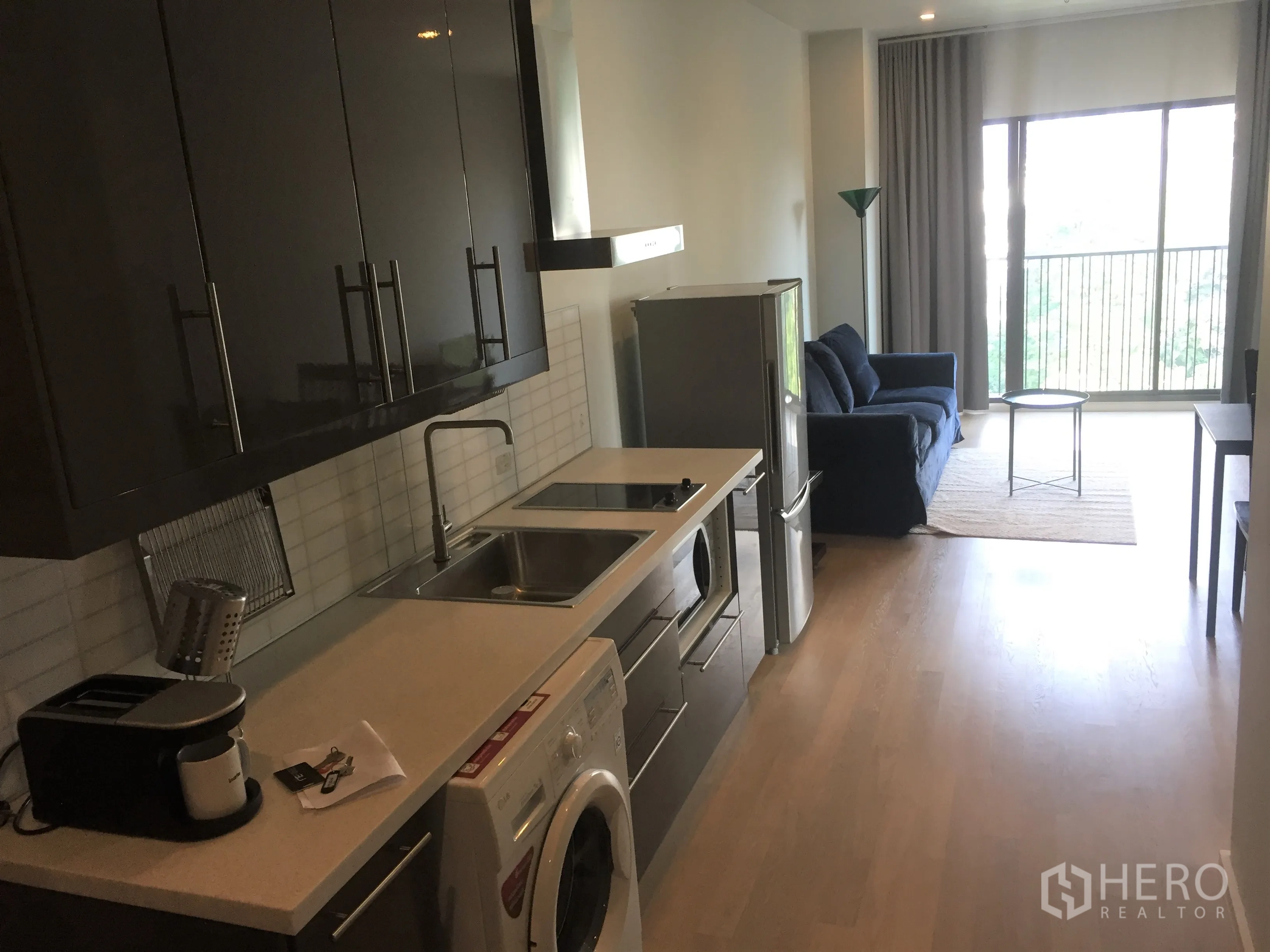 Condominium for rent in Bangkok - Open-plan kitchen and living area with appliances, sofa and balcony access.