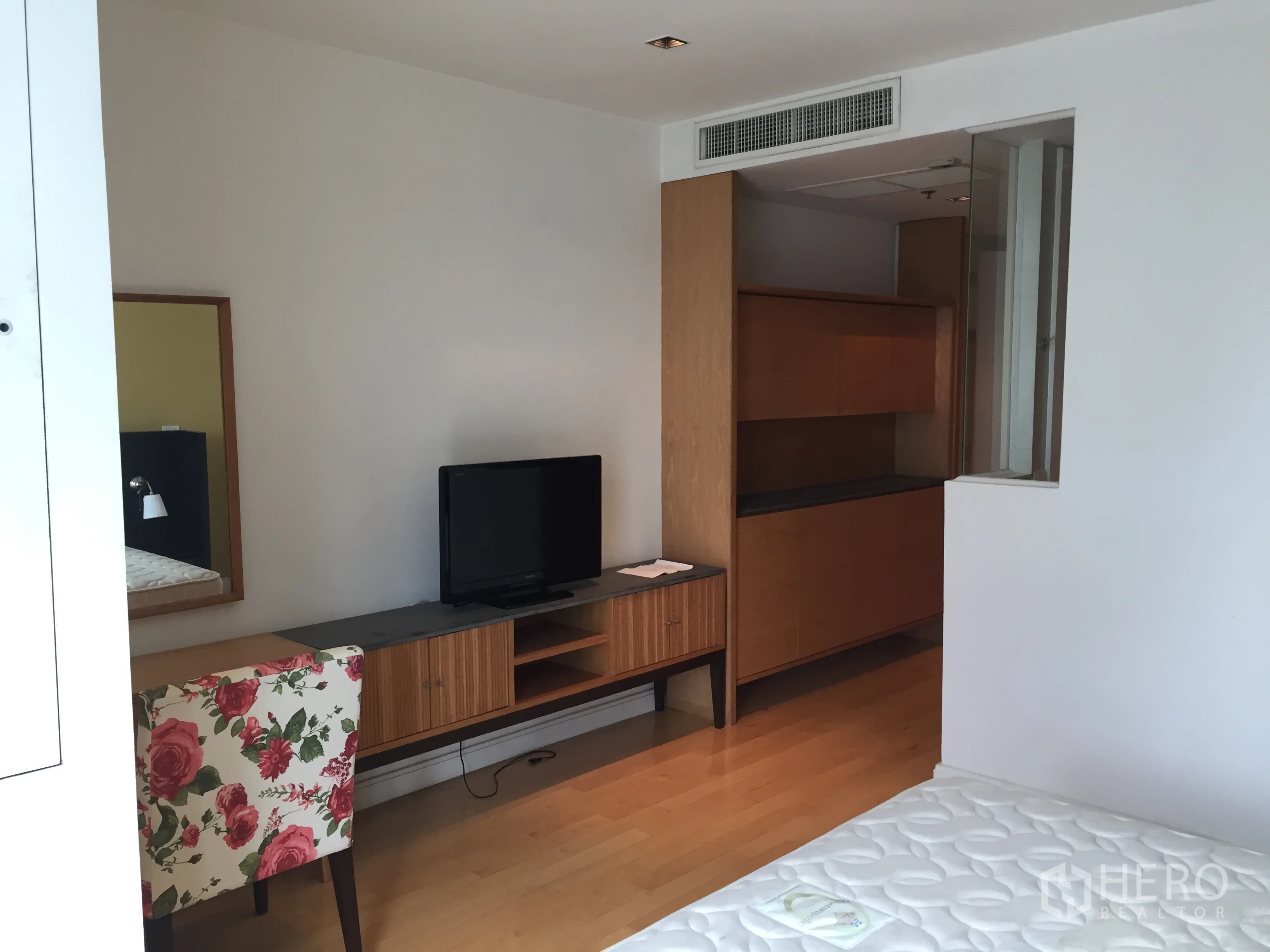 公寓 出租或出售在Pathum Wan, Bangkok - 明亮卧室一角，电视柜、花卉单椅与内置收纳。