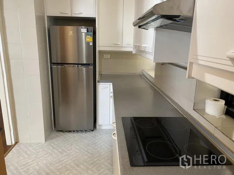 Condominium for rent or sale in Sathon, Bangkok - Modern kitchen with electric cooktop, range hood, stainless-steel refrigerator and long counters.