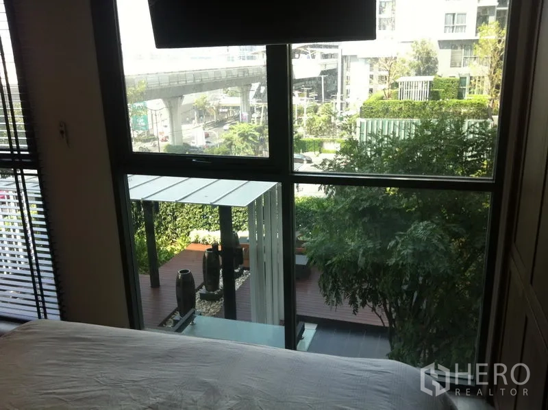 Condominium for rent in Phra Khanong, Bangkok - View from bedroom over landscaped courtyard toward an elevated transit line and city surroundings.
