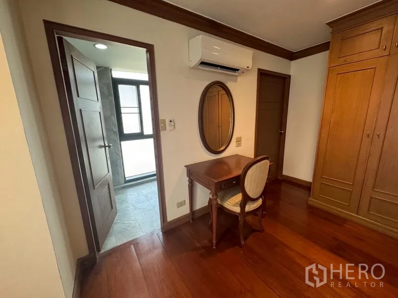 Condominium for rent in Watthana, Bangkok - Bedroom corner with writing desk, mirror, and doorway to the bathroom.