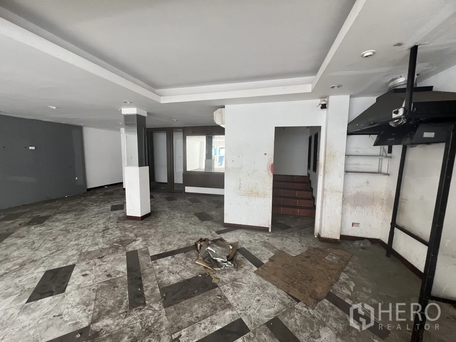 Shophouse for rent in Khlong Toei, Bangkok - Ground-floor retail space showing recessed lighting, a staircase to upper levels and worn tile floors ready for renovation.