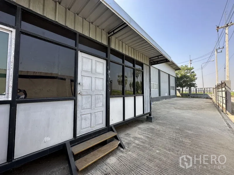 Factory for rent in Lam Luk Ka, Pathum Thani - Front modular office facade with glass panels and steps beside wide driveway.