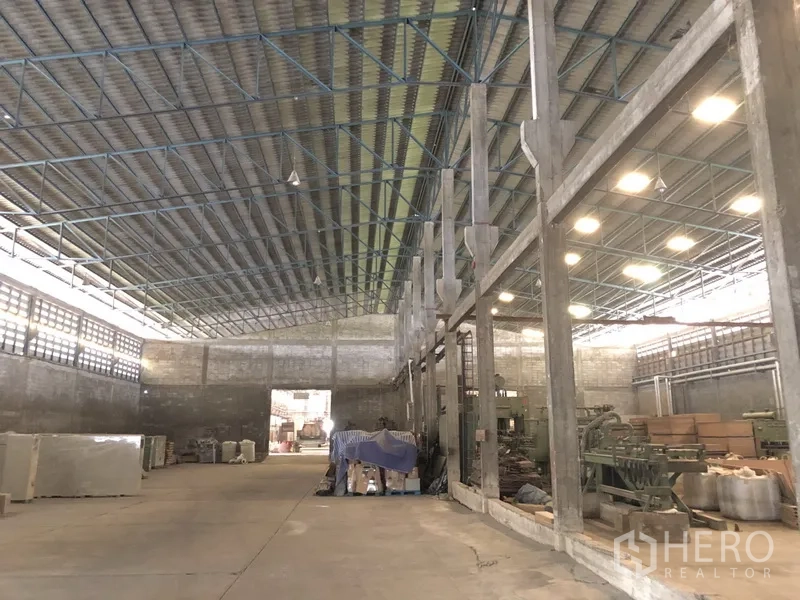 Factory for rent in Bang Bua Thong, Nonthaburi - Expansive production hall with high steel truss roof, skylights, and concrete floor.