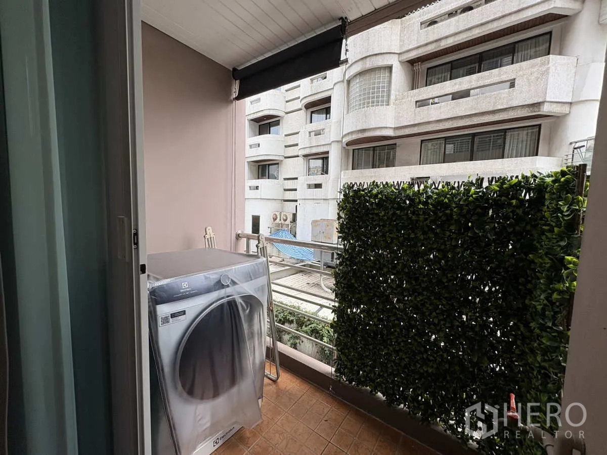Condominium for rent in Khlong Toei, Bangkok - Private balcony with washing machine and green privacy screen facing neighboring buildings.
