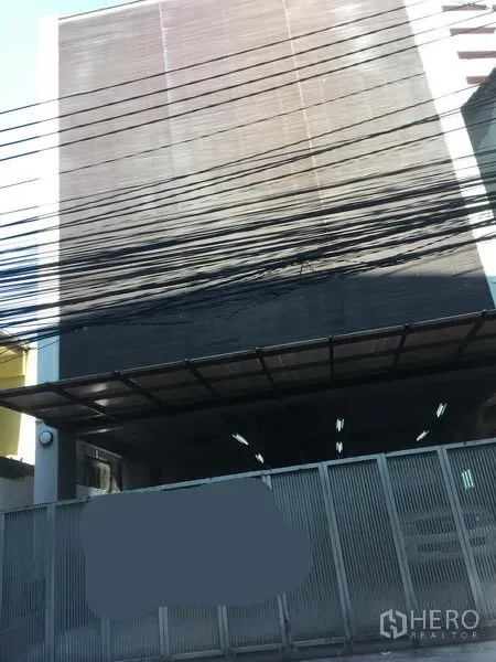 带办公室的家 出租在Watthana, Bangkok - 多层家庭式办公楼，带金属安全大门与雨棚入口，城市小巷上空有电缆。