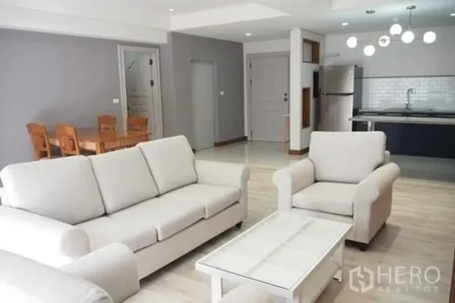 Condominium for rent in Pathum Wan, Bangkok - Bright open-plan living room with white sofas, coffee table and view to the modern kitchen.