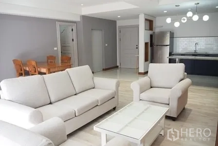 Condominium for rent in Pathum Wan, Bangkok - Bright open-plan living room with white sofas, coffee table and view to the modern kitchen.