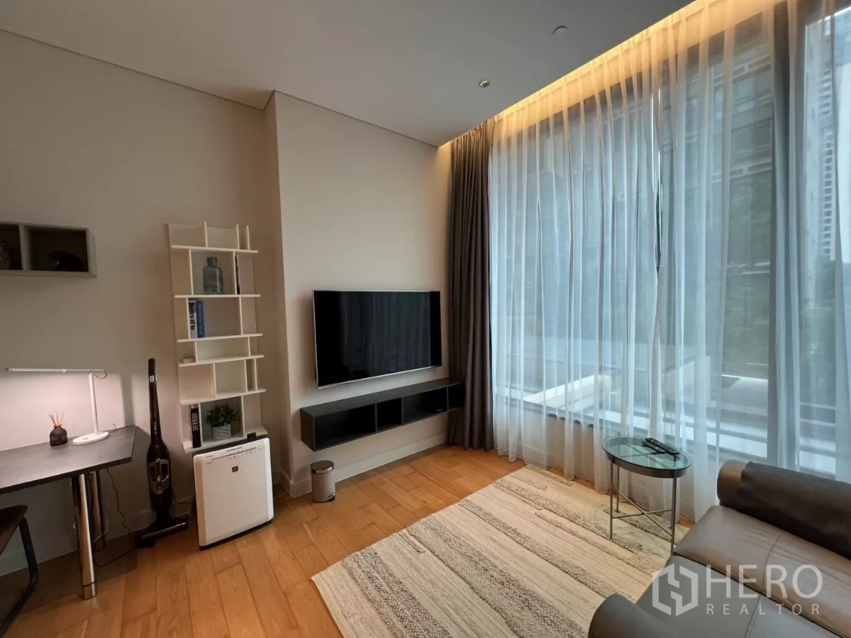 公寓 出租在Pathum Wan, Bangkok - 明亮客厅的电视墙与书桌，搭配落地窗纱帘。