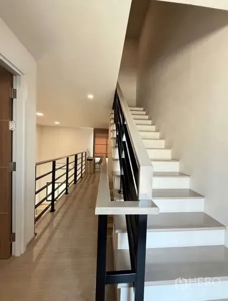 Townhouse for rent in Bang Phli, Samut Prakan - Staircase with black metal railing leading to a mezzanine hallway in the townhouse.