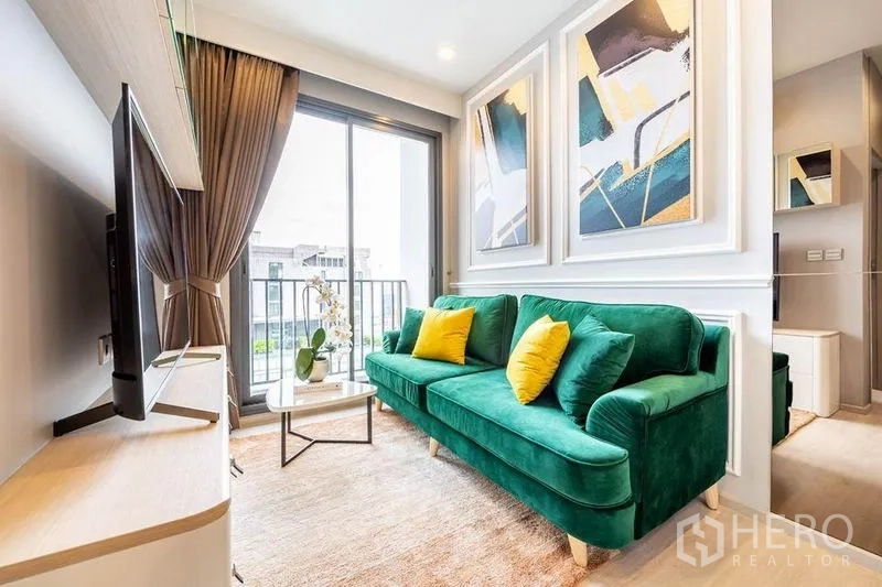 Condominium for rent or sale in Watthana, Bangkok - Bright living room with green sofa, sliding balcony door and abstract wall panels.