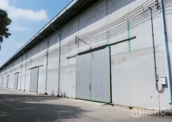 Warehouse for rent in Prawet, Bangkok - Row of concrete warehouse units in Prawet, Bangkok with large sliding metal doors and driveway.