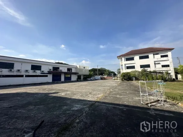 Warehouse for rent in Khlong Sam Wa, Bangkok - Large open parking and turning area beside low‑rise warehouse and office buildings.