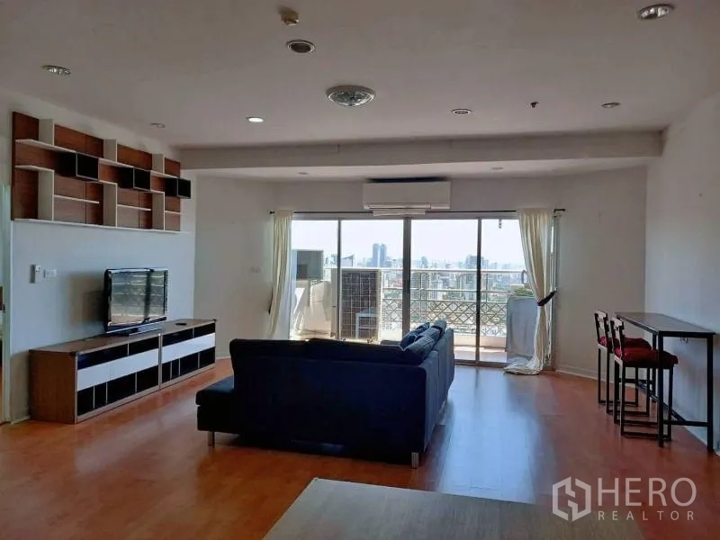 Condominium for rent in Khlong Toei, Bangkok - Spacious living area facing large sliding doors to a balcony with city skyline view and a bar table.