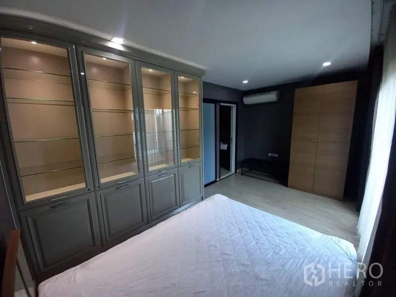 Townhouse for rent in Suan Luang, Bangkok - Bedroom featuring wall-to-wall illuminated glass display cabinets and air conditioning.