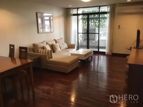 公寓 出租在Watthana, Bangkok - 通罗公寓客厅，木地板、转角沙发，推拉门通向绿意阳台