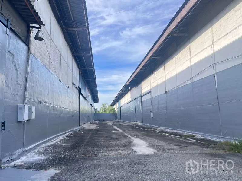 Factory for rent in Bang Pakong, Chachoengsao - Paved loading driveway between two gray warehouse buildings with metal roofs and roller doors in Bang Pakong.