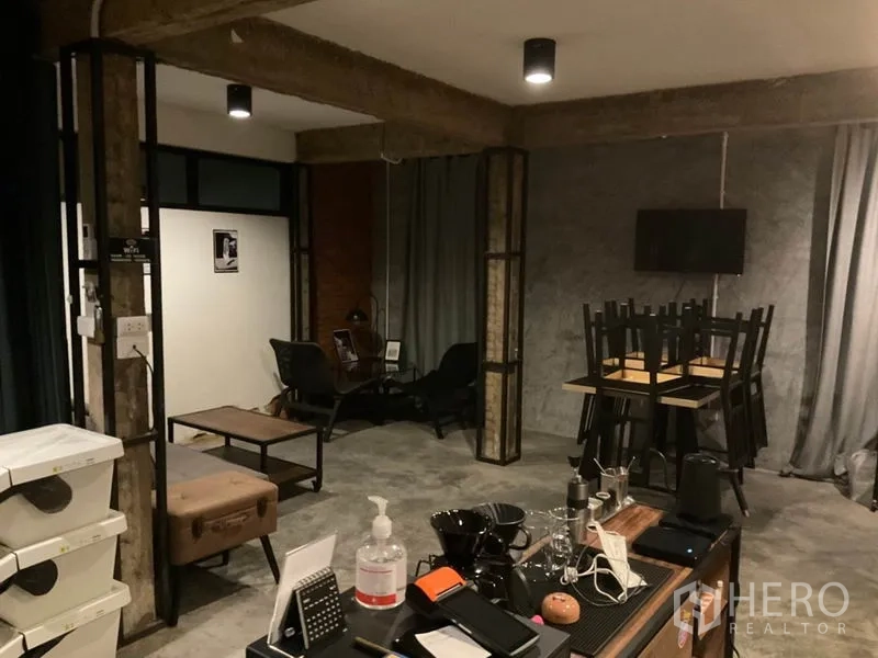 Home Office for rent in Phaya Thai, Bangkok - Loft-inspired office showing counter workspace with coffee gear, exposed beams, lounge corner, stacked chairs and polished concrete flooring.
