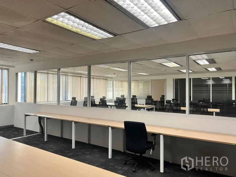 办公空间 出租在Khlong Toei, Bangkok - 室内长条工作台沿玻璃内窗布置，分隔两个办公区的视线。