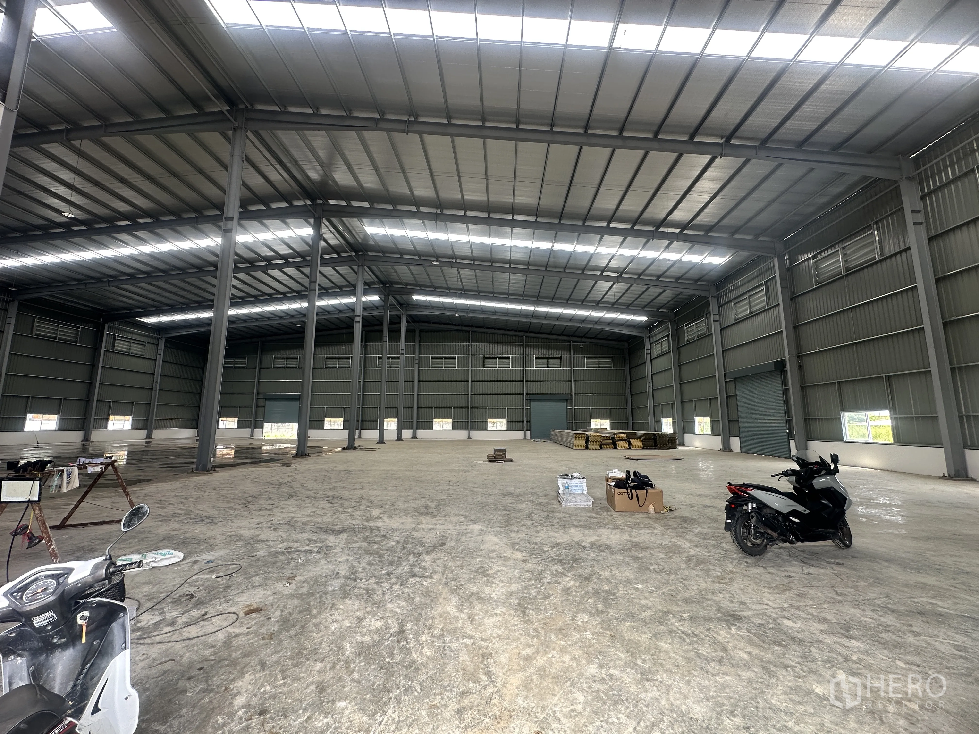 Warehouse for rent or sale in Lam Luk Ka, Pathum Thani - Open warehouse hall with a steel frame, skylight panels, and materials on the floor.