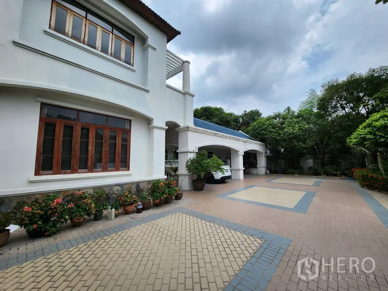 บ้าน ให้เช่าในPrawet, Bangkok - ลานจอดรถกว้างหน้าบ้านเดี่ยวสีขาวสองชั้น มีซุ้มทางเข้าและต้นไม้กระถางจัดแต่งสวยงาม