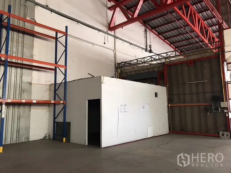 Warehouse for rent in Bang Na, Bangkok - Utility room beside large metal sliding door and empty racking inside warehouse.