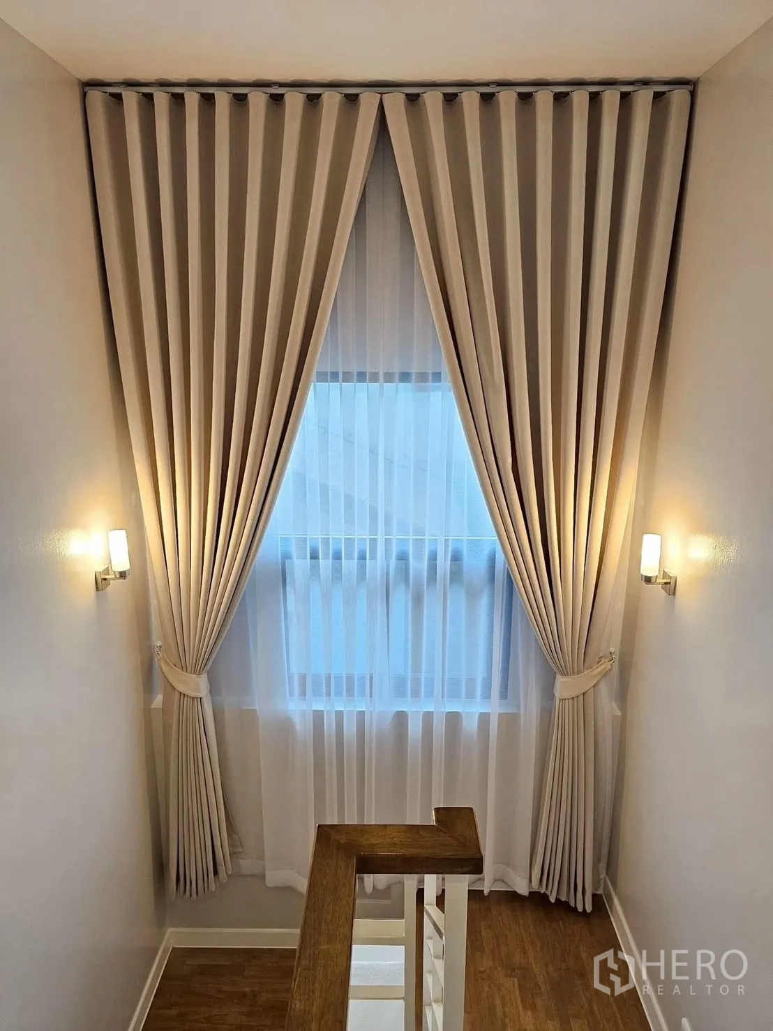 独立式住宅 出售在Bang Phli, Samut Prakan - 楼梯平台，木质扶手，高窗配遮光帘与纱帘，壁灯柔光。