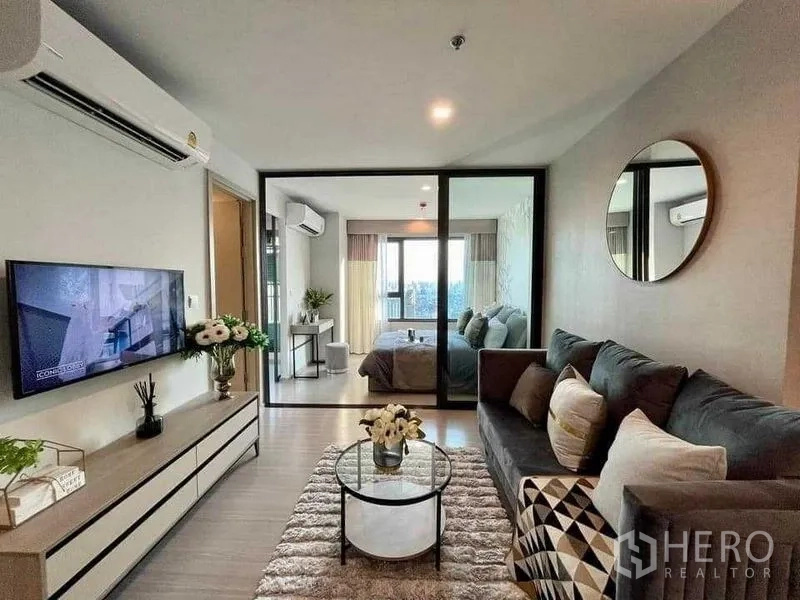 Condominium for rent in Chatuchak, Bangkok - Bright living room with sofa, TV console and a glass partition leading to the bedroom.