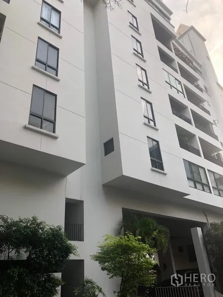 Condominium for sale in Watthana, Bangkok - Modern mid-rise condominium exterior with balconies and landscaped greenery.