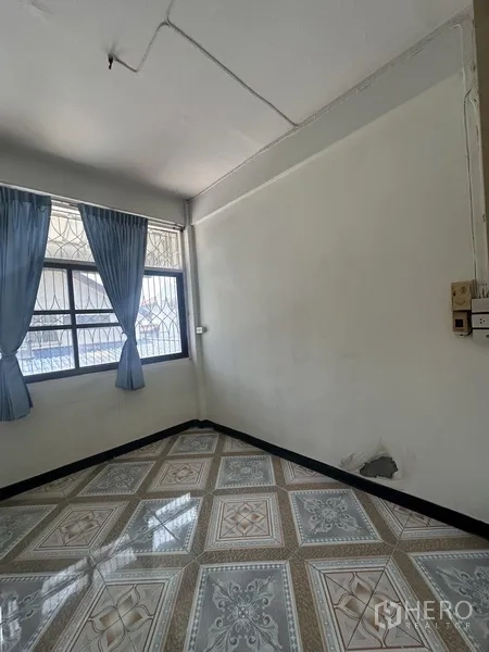 Shophouse for rent or sale in Phra Khanong, Bangkok - Compact room with patterned tile floor, barred window, and blue curtains.