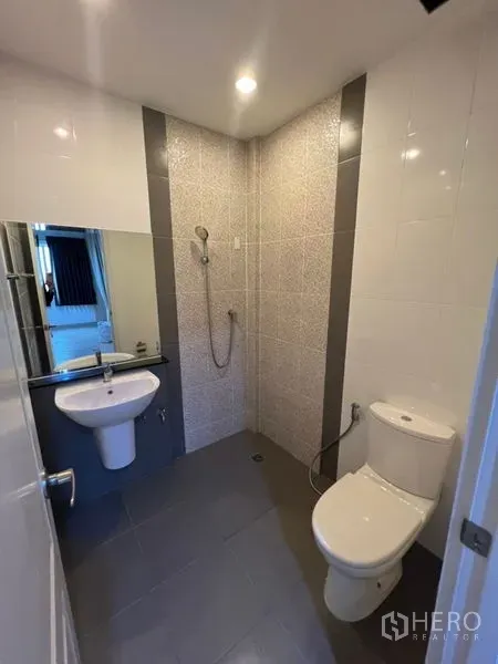 Home Office for rent - Compact tiled bathroom featuring walk-in shower, toilet, sink, and large mirror.