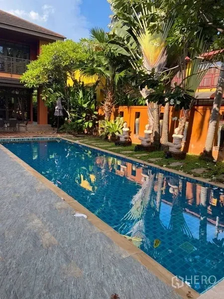 Detached House for rent in Suan Luang, Bangkok - Long blue-tiled lap pool bordered by lush greenery and the villa’s orange exterior.